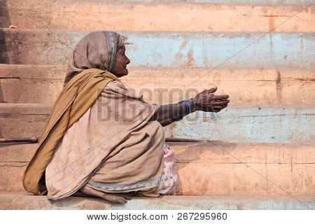 BENARES, VARANASI, UTTAR PRADESH, INDIA - FEBRUARY 06, 2013: unknown poor woman begs for money from a passerby on the street in Benares during Kumbh Mela festival