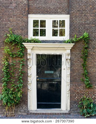 Old Black Wooden Door With White Frame On Brown Brick Wall.
