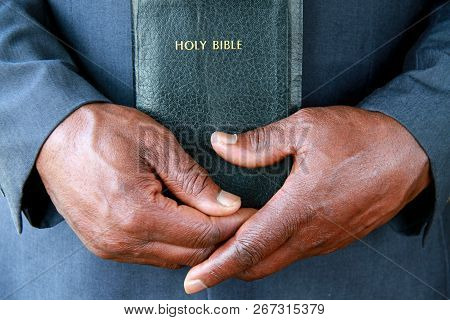 Black Man Praying With Hands Clasped Together Holding The Holy Bible After Prayer At A Service In Ch
