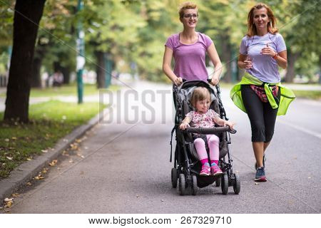two young healthy women jogging together while pushing a baby stroller at city park