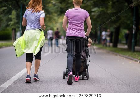two young healthy women jogging together while pushing a baby stroller at city park