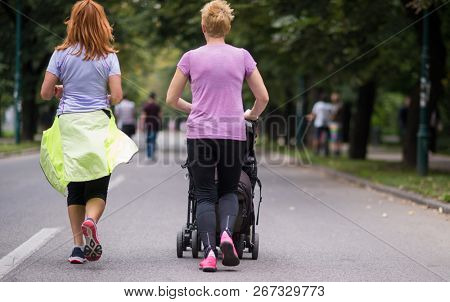two young healthy women jogging together while pushing a baby stroller at city park