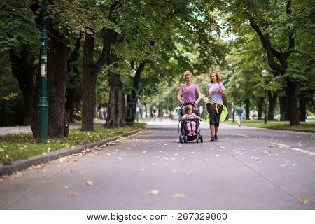 two young healthy women jogging together while pushing a baby stroller at city park