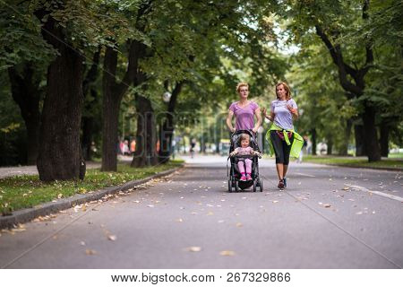 two young healthy women jogging together while pushing a baby stroller at city park