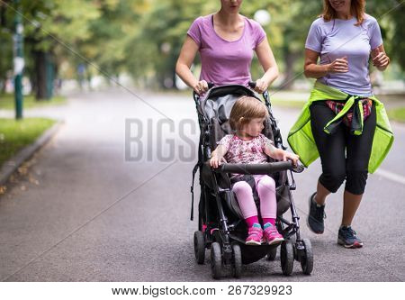 two young healthy women jogging together while pushing a baby stroller at city park