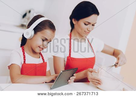 Girl With Headphones Looks How Bake A Cake. Love Mother Help Daughter With Bake. Dother Looks How Do