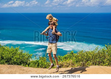 Dad And Son Travelers On A Cliff Above The Beach. Empty Paradise Beach, Blue Sea Waves In Bali Islan