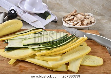 Ribbons Of Thin Sliced Zucchini And Yellow Squash On A Cutting Board With A Mandolline Slicer