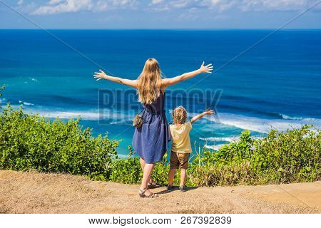 Mom And Son Travelers On A Cliff Above The Beach. Empty Paradise Beach, Blue Sea Waves In Bali Islan