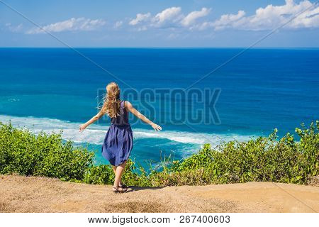 Young Woman Tourist On A Cliff Above The Beach. Empty Paradise Beach, Blue Sea Waves In Bali Island,