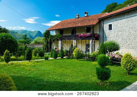 Picturesque Courtyard Of The Monastery Of Moraca With Green Grass Lawn, Flowers And Buildings With R