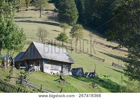 The Old Ukrainian Hut With A Slate Roof And A Wooden Fence In A Green Field