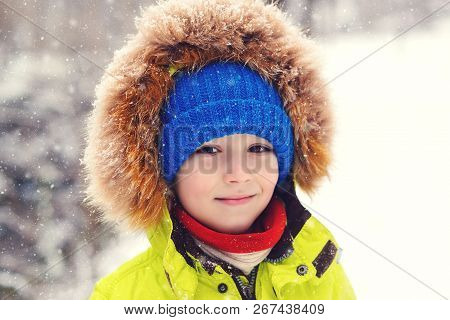 Cute Child Boy In Winter Clothes Outdoors. Portrait Of Happy Little Boy Playing Under Snow. Happy Ki