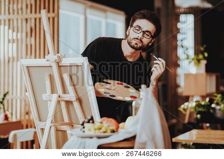 Painter Holds Palette Looking At Still Life. Portrait Of Talanted Young Caucasian Man Painting With 