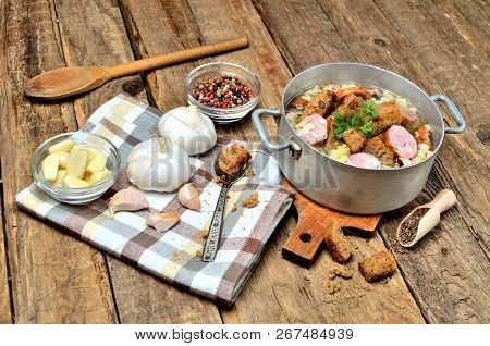 Close-up Of Garlic Soup In An Old Saucepan, Fresh Garlic Bulbs, Cloves, Colored Pepper, Wooden Spoon