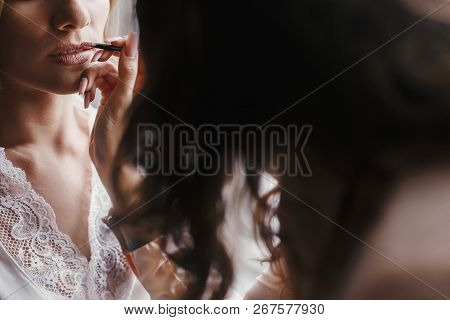 Stylish Bride Getting Her Make-up In The Morning At Window Light. Makeup Artist Painting  Lips With