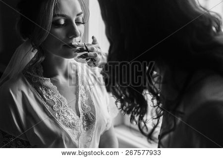 Stylish Bride Getting Her Make-up In The Morning At Window Light. Makeup Artist Painting  Lips With
