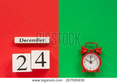 Wooden Calendar December 24th And Alarm Clock On Red And Green Background. Top View Flat Lay Concept