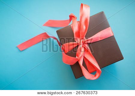Brown Gift Box With Red Ribbon On Blue Background. Top View With Copy Space.