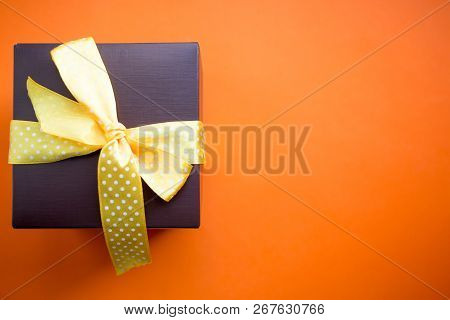 Brown Gift Box With Yellow Ribbon On Orange Background. Top View With Copy Space.