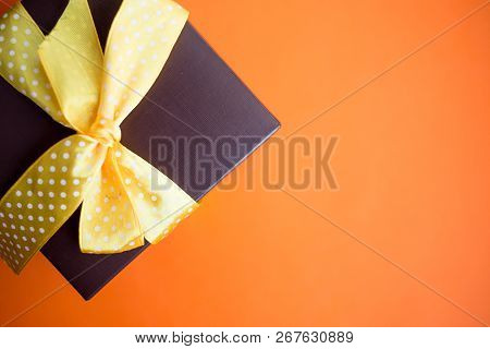 Brown Gift Box With Yellow Ribbon On Orange Background. Top View With Copy Space.