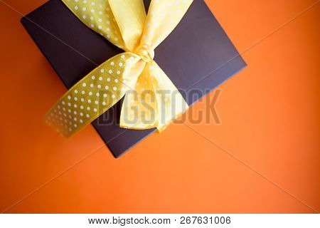 Brown Gift Box With Yellow Ribbon On Orange Background. Top View With Copy Space.