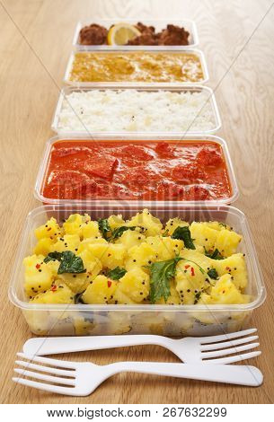 A Selection Of Indian Takeaway Food In Plastic Containers On A Wooden Table. Aloo Saag Potato Spinac