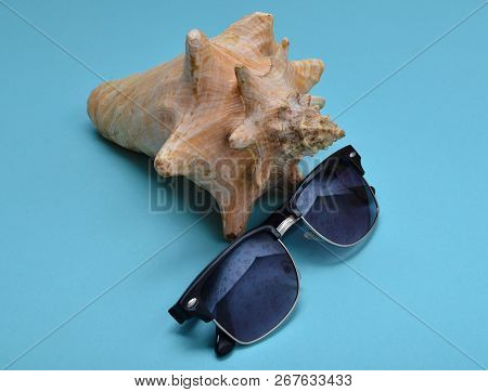 Decorative Seashell And Sunglasses On A Blue Paper Background. The Concept Of A Resort Holiday.