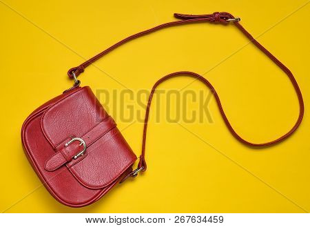Red Leather Bag On A Long Strap On A Yellow Background. Women's Accessories. Top View.