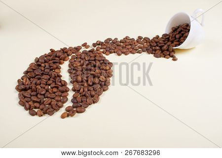 Roasted Brown Coffee Beans Falling Out Of White Porcelain Cup Forming A Shape Of A Big Coffee Bean. 