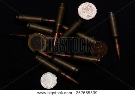 One Euro, One Russian Ruble And Ukrainian Hryvna Coins With Rifle Military Ammo On Black Background.
