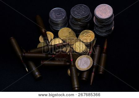 One Euro And Small Ukrainian Coins With Rifle Military Ammo On Black Background. Symbolizes War For 