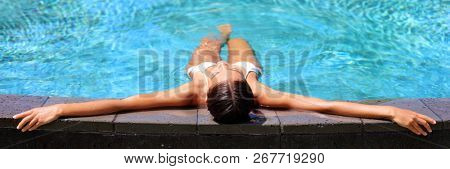Luxury resort woman relaxing in infinity swim pool. Asian young adult lying down in swimming pool of beach resort for summer holidays or travel vacations banner.