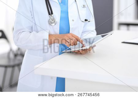 Close-up Of Female Physician Using Digital Tablet  While Standing Near Reception Desk At Clinic Or E