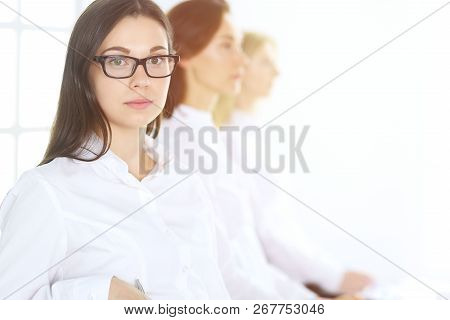 Attractive Businesswoman At Meeting Or Conference Against The Background Of Colleagues. Group Of Bus