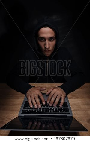 Portrait Of Hacker In Black Hoodie Looking At Camera While Using Laptop, Cuber Security Concept