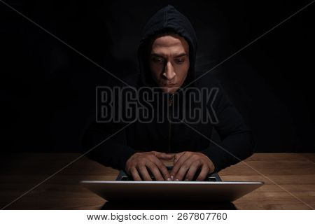 Portrait Of Concentrated Hacker In Black Hoodie Using Laptop, Cuber Security Concept