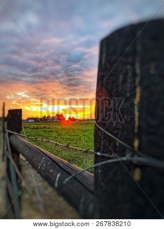 The Focus Of The Sunset, As The Wooden Post Is In Subtly Blur On The Outside Frame