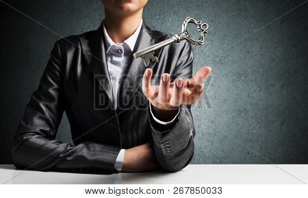 Cropped Image Of Businessman In Suit Keeping Big Key In Hand With Dark Wall On Background.