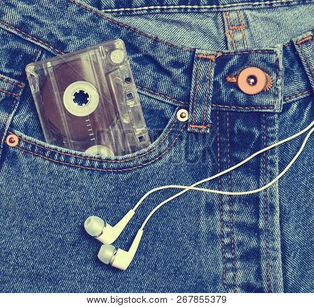 Audio Cassette In A Pocket Of Old-fashioned Blue Jeans And Headphones Isolated On A White Background