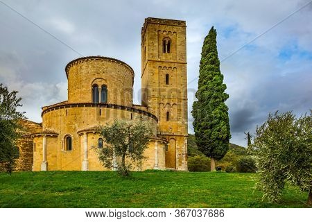Picturesque Tuscany. Ancient magnificent abbey of San Antimo. Tall slender cypress adorns  the abbey. Autumn day. The concept of active, rural and photo tourism