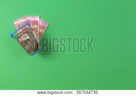 Top View To Mini Shopping Trolley With Euro Coints And Euro Banknotes Over Green Background. Shoppin