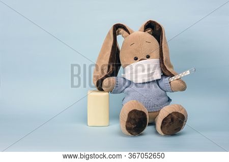 Soft Toy Sits In Protective Medical Mask On Blue Background. Protective Mask Protects Against Coronv