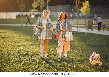 Two Girls Wallking In A Park With A Little Dog