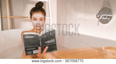 Woman reading book in warm bathtub taking a bath relaxing at home - pamper wellness Asian girl pampering skin care with facial mask treatment banner panorama.