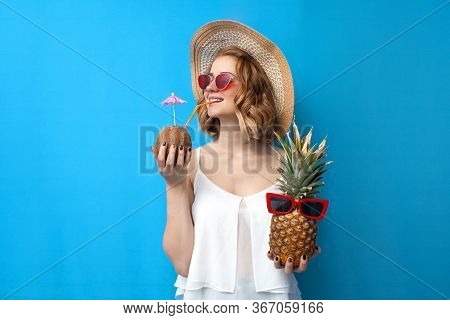 Girl In A Sun Hat And Glasses Drinks Tropical Cocktails Made Of Pineapple And Coconut On A Blue Isol