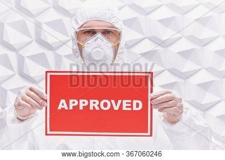 COVID-19 concept. A doctor in a protective suit holds a sign approved on a white background. Copy space.