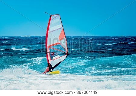 Summer Sports: A Surfer With Red And Blue Sail Riding The Wave During A Sunny Summer Afternoon On Th