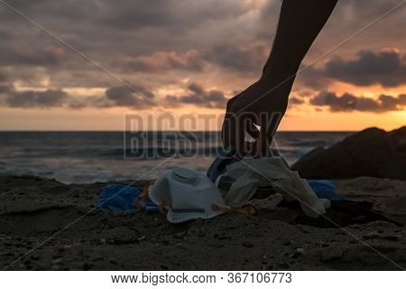 Man Habd Collect Medical Waste, Mask And Plastic Gloves Garbage Trash On Sunset Sea Shore, Coronavir