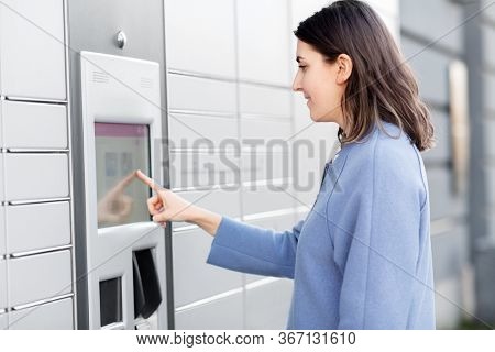mail delivery and post service concept - happy smiling woman choosing operation on outdoor automated parcel machine's touch screen